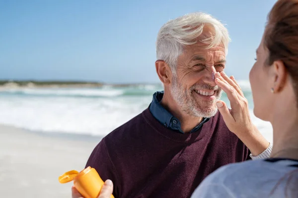 노인의 얼굴은 자신의 아내가 자외선 차단제를 바르는 남편은 해변에서 얼굴에 — 스톡 사진