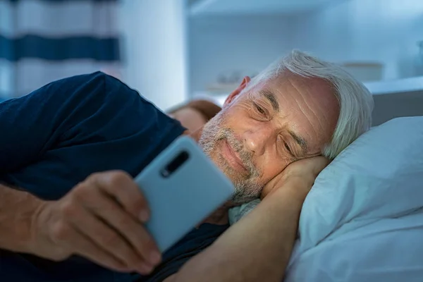 선배가 침대에 스마트폰으로 비디오를 있어요 침대에 속에서 핸드폰을 사용하는 남자를 — 스톡 사진
