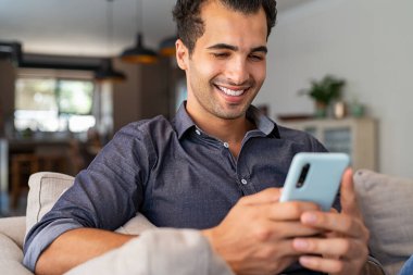 Neşeli iş adamı evdeki kanepede otururken akıllı telefon kullanıyor. Kanepede oturan yakışıklı genç Hintli adam cep telefonundan mesajlar okuyor. Evde cep telefonuyla çalışan İspanyol bir adam..