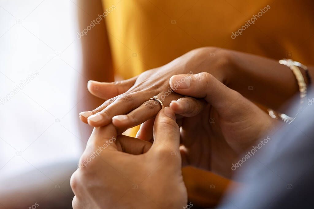 Close up of man putting beautiful engagement ring on his girlfriend hand. Man is making marriage proposal with golden ring with diamond to his woman. Close up hands of indian guy giving an engagement ring: do you want to marry me?
