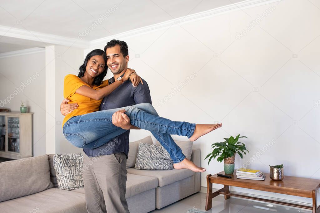 Romantic young middle eastern man lifting woman holding in hands. Joyful couple moving into their new home with husband carrying his wife. Man carrying indian woman in his arms moving in booking house for vacation.