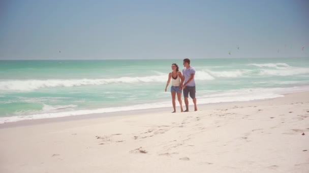 快乐的年轻夫妇手牵手 赤脚在沙滩上散步 并留有复制的空间 一个英俊的男人和一个漂亮的女人在海滨随便玩乐和开玩笑 快乐的一对微笑的情侣在白沙滩的海滨放松 — 图库视频影像