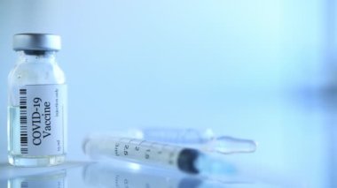 Laboratuvardaki COVID-19 koronavirüs aşı tüplerini kapatın. Sars-CoV-2 aşılı şırınga ve şişe klinik deneye hazır. Şişede bir doz aşı, cam sehpanın üzerinde de fotokopi alanı var..