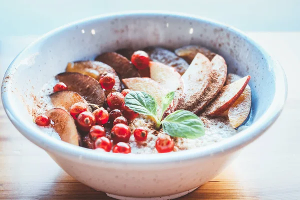 Best healthy vegan breakfast. Organic oatmeal porridge in a white ceramic bowl with apple, cinnamon, red berries. Healthy breakfast. Diet concept. Close up.