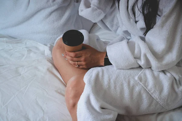 Ένα νεαρό κορίτσι με λευκό μπουρνούζι κρατάει ένα φλιτζάνι καφέ. Πρωινή ώρα. Νύφη. Μανικιούρ. Δαχτυλίδι στο δάχτυλό της. Ώρα Σαββατοκύριακου. — Φωτογραφία Αρχείου