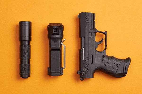 self defense and security equipment - pistol, pepper spray and tactical flashlight on orange background