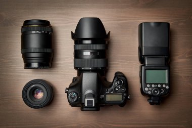 Modern dijital kamera ekipmanlarının üst görüntüsü - Zoom lensi ve kaputu olan DSR, ahşap masa üzerinde lensler ve harici el feneri