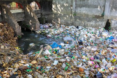 Plastic bottles and takeaway food containers carelessly thrown away into a sewage water system in an asian market place