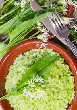 Ramsonlar (yaban sarımsaklı pırasa) parmesan peynirli risotto, kırmızı bir tencerede servis edilir ve taze Ramson yaprakları ve çiçekler