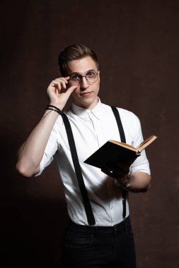 Yuvarlak gözlüklü, askılı, beyaz gömlekli bir adam kitap okuyor..