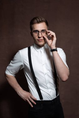 Yuvarlak gözlüklü, askılı ve beyaz gömlekli bir adam..