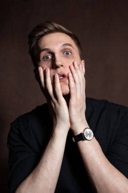 A man in round glasses and a black shirt is grimacing