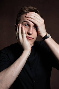A man in round glasses and a black shirt is grimacing