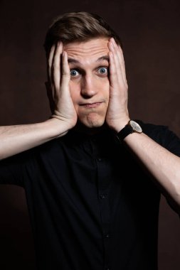 A man in round glasses and a black shirt is grimacing