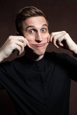A man in round glasses and a black shirt is grimacing