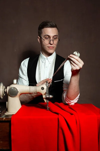 Alfaiate em copos redondos senta-se em uma mesa com uma máquina de costura — Fotografia de Stock
