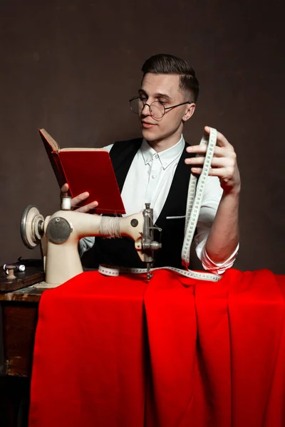 Alfaiate em copos redondos senta-se em uma mesa com uma máquina de costura — Fotografia de Stock