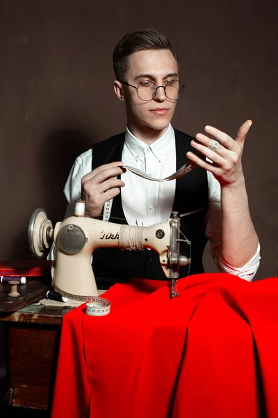 Alfaiate em copos redondos senta-se em uma mesa com uma máquina de costura — Fotografia de Stock