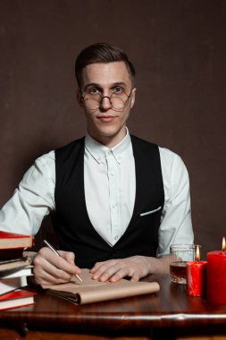 Yuvarlak gözlüklü bir adam kitap yazıyor.