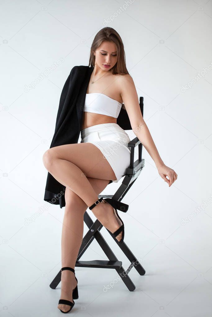 girl in white with a black jacket sits on a chair, light background