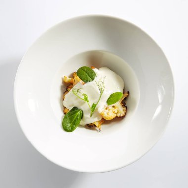 Krem soslu fırında karnabahar ve taze yeşillikler izole edilmiş.