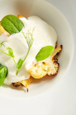 Krem soslu fırında karnabahar ve taze yeşillikler izole edilmiş.