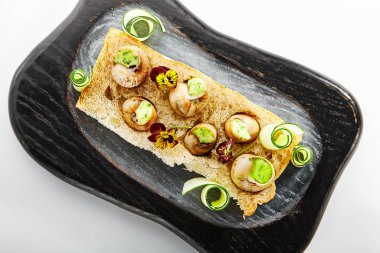 Sarımsak ve peynir kaplı salyangozlar. Soslu leziz salyangozlar. Ahşap tepside yemek tabağı. Ekmeğin üstünde menekşelerle servis edilen lezzetli bir yemek. Fransız yemek sunumu, mutfak menüsü