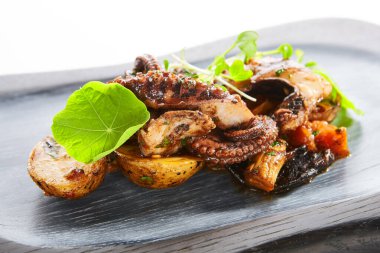 Fırında patates ile ızgara ahtapot. Lezzetli deniz ürünleri yakın çekim manzarası. Yeşillik ve kızarmış sebzeli lezzetli bir yemek. Tabaktaki yemek bileşimi. Restoran yemeği, aşçılık sunumu.