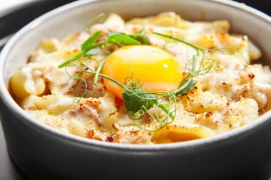 Fırınlanmış carbonara yakın çekim görüntüsü. Yumurtalı makarna, peynir ve taze yeşillik. Geleneksel İtalyan yemeği. Lezzetli yemek kompozisyonu, mutfak sunumu. Avrupa mutfağı, lezzetli servis edilen yemekler.