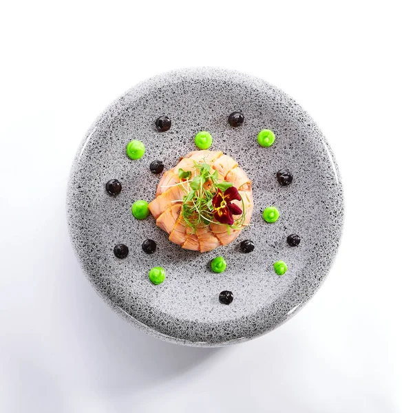 Salmon olivier salad with sauces. Sliced fish dish with greenery. Tasty seafood decorated with violet flower. Haute cuisine on plate. Restaurant meal, elegant food composition