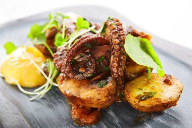 Fırında patates ile ızgara ahtapot. Lezzetli deniz ürünleri yakın çekim manzarası. Yeşillik ve kızarmış sebzeli lezzetli bir yemek. Tabaktaki yemek bileşimi. Restoran yemeği, aşçılık sunumu.