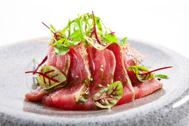 Tataki ton balığı yakın çekim görüntüsü. Geleneksel Japon mutfağı metodu. Tabakta lezzetli balıklar var. Yeşillik ve baharatlı dilimlenmiş deniz ürünleri. Asya mutfağı, yemek kompozisyonu. Restoran yemeği.