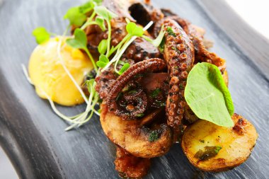 Fırında patates ile ızgara ahtapot. Lezzetli deniz ürünleri yakın çekim manzarası. Yeşillik ve kızarmış sebzeli lezzetli bir yemek. Tabaktaki yemek bileşimi. Restoran yemeği, aşçılık sunumu.