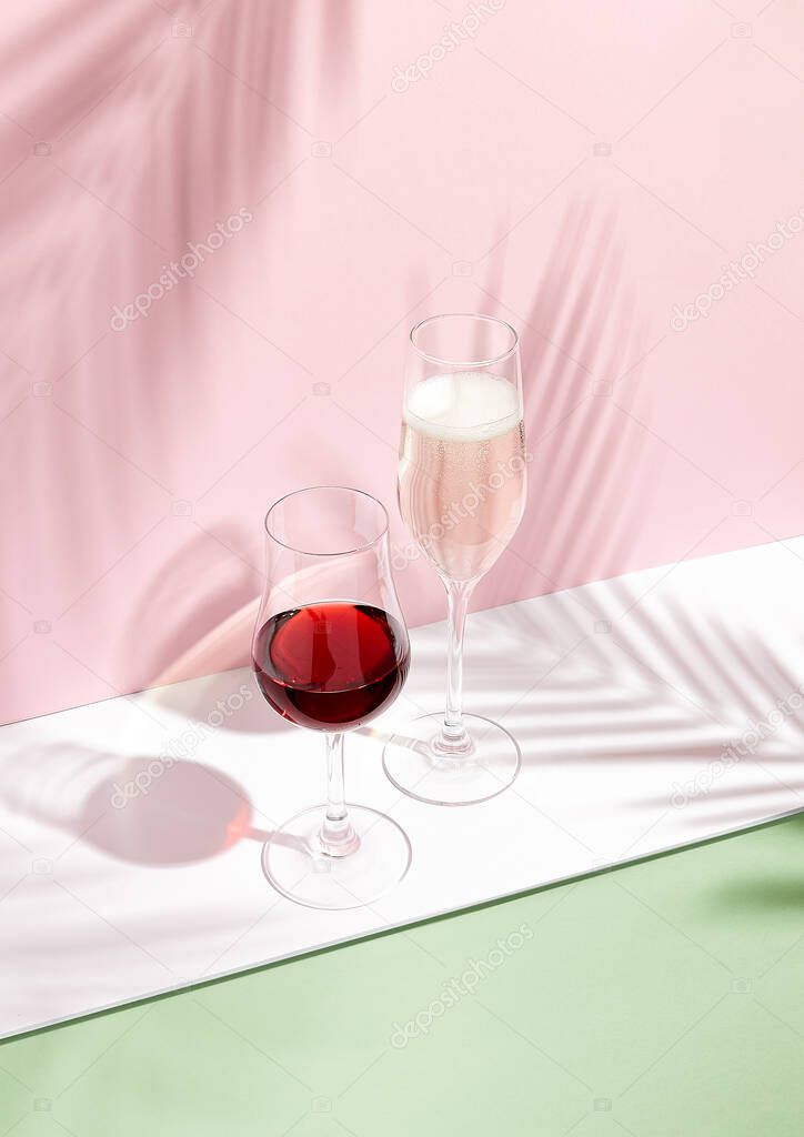 Champagne and red wine on creative background. Shadows of palm leaf on pink walls and white floor. Pink, white and green. 