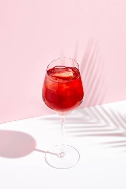 Yaratıcı arka planda şarap kadehiyle kırmızı yaz kokteyli. Pembe duvarda ve beyaz zeminde palmiye yaprağının gölgeleri. 