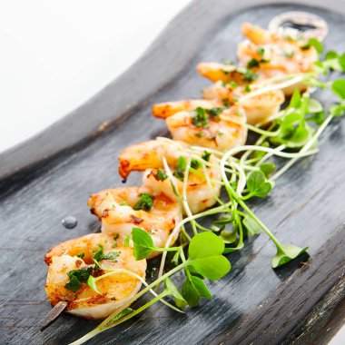 Karides kebabı yakın çekim görüntüsü. Yeşillikli lezzetli deniz ürünleri. Ahşap tepside bahçe tereli kavrulmuş karides. Mutfak sunumu, yemek kompozisyonu. Lezzetli restoran yemeği, haute cuisine