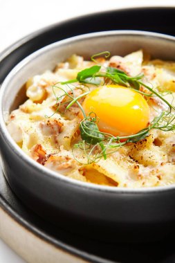 Fırınlanmış carbonara yakın çekim görüntüsü. Yumurtalı makarna, peynir ve taze yeşillik. Geleneksel İtalyan yemeği. Lezzetli yemek kompozisyonu, mutfak sunumu. Avrupa mutfağı, lezzetli servis edilen yemekler.