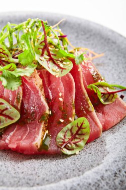 Tataki ton balığı yakın çekim görüntüsü. Geleneksel Japon mutfağı metodu. Tabakta lezzetli balıklar var. Yeşillik ve baharatlı dilimlenmiş deniz ürünleri. Asya mutfağı, yemek kompozisyonu. Restoran yemeği.