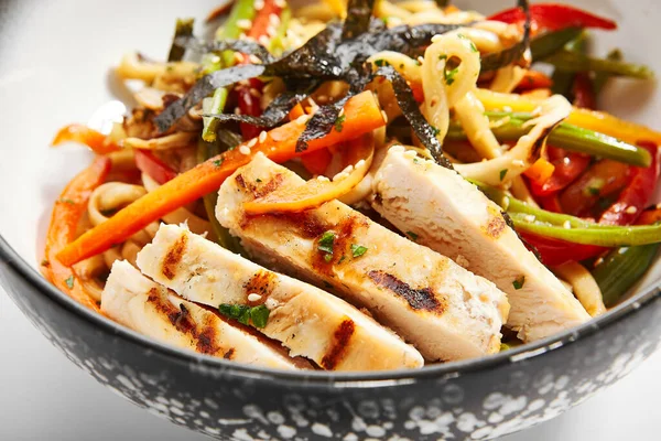 Wok udon with vegetables and chicken closeup view. Traditional asian meal on white table. Delicious dish with sliced meat, carrot and pepper. Tasty noodles with seasonings. Food composition