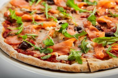 Somonlu dilimlenmiş pizza, kalamata zeytin ve kurutulmuş domates. Geleneksel İtalyan mutfağı. Taze roka ile süslenmiş lezzetli pişmiş yemek. Avrupa tarifi, gıda sunumu