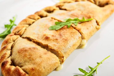 Parma jambonlu Calzone pizza, domates ve mozzarella. Fırında pişmiş roka ile katlanmış pizza. Geleneksel İtalyan mutfağı. Cheeze ve yeşillikle dilimlenmiş fast food. Lezzetli aromatik yemek.