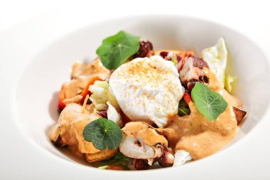 Beyaz kasede salata. Dilimlenmiş ahtapot ve kızarmış patates. Mayonez, domates baharatlı jajika ve ev yapımı füme biber sosu ile servis edilmiş. Restoran yemekleri tabakta. Kapatın.