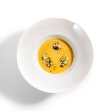 Beyaz kasede balkabağı çorbası. Ana yemek üst görüntüde servis edildi. Tohumlarla süslenmiş sebze kremalı çorba. Restoran yemek bölümü, ana yemek. Vejetaryen yemeği. Akşam yemeği, tabakta gurme yemeği.