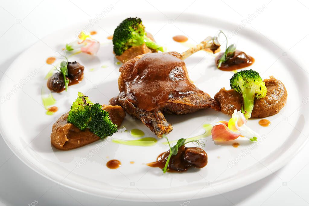 Confit duck leg with vegetables. Served meat with smoked cabbage puree and roasted broccoli. Restaurant food portion, main course in white plate close up. Cooked supper, plated dish