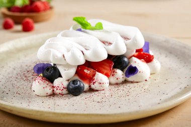 Beyaz seramik tabakta Pavlova tatlısı. Kremalı pasta, kremalı pastane. Kapatın. Krem şanti, yabanmersini ve çilekli hamur işi. Nane ve menekşe yapraklı gurme mezeleri.