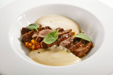 Sığır kalbi yahnisi ve sebzeler. Kızarmış et ve sebzeli risotto beyaz arka planda izole edilmiş tabakta servis edildi. Gurme aşçılık, gastronomi. Restoran yemekleri, ana yemek.