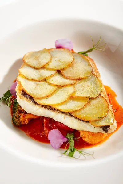 Fried flounder fillet on baked potato slices. Served luxury cuisine. Fish with tomato and olives ragout in white plate isolated. Restaurant high menu food portion. Delicious supper, main course