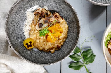 Beyaz mantarlı risotto ve gri kaseli balkabağı. İtalyan pilav lapası. Yakından. Menekşe çiçekli ve yeşil süslemeli lezzetli geleneksel yemekler. Restoran yemeği, şarküteri.