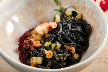 Bej kasede karides ve kabaklı siyah spagetti. Mürekkepbalıklı makarna yakından. Lezzetli şarküteri, servis edilen restoran yemeği, deniz ürünleri ve sebzeli lezzetli erişte.