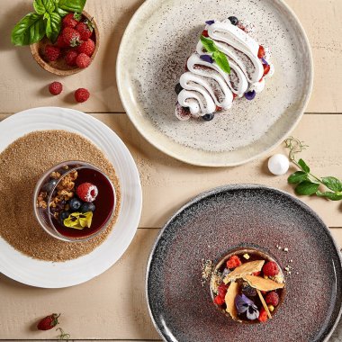 Seramik tabaklar üzerinde lezzetli tatlılar. Pavlova, Panna Cotta ve Tart. Tatlı yemek, şekerli fırın, krem şanti ve böğürtlen süslemeli kremalı pasta. Tahta masada lezzetli pastalar ikram ettim.